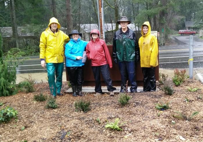 5 people in rain coats standing in garden beds