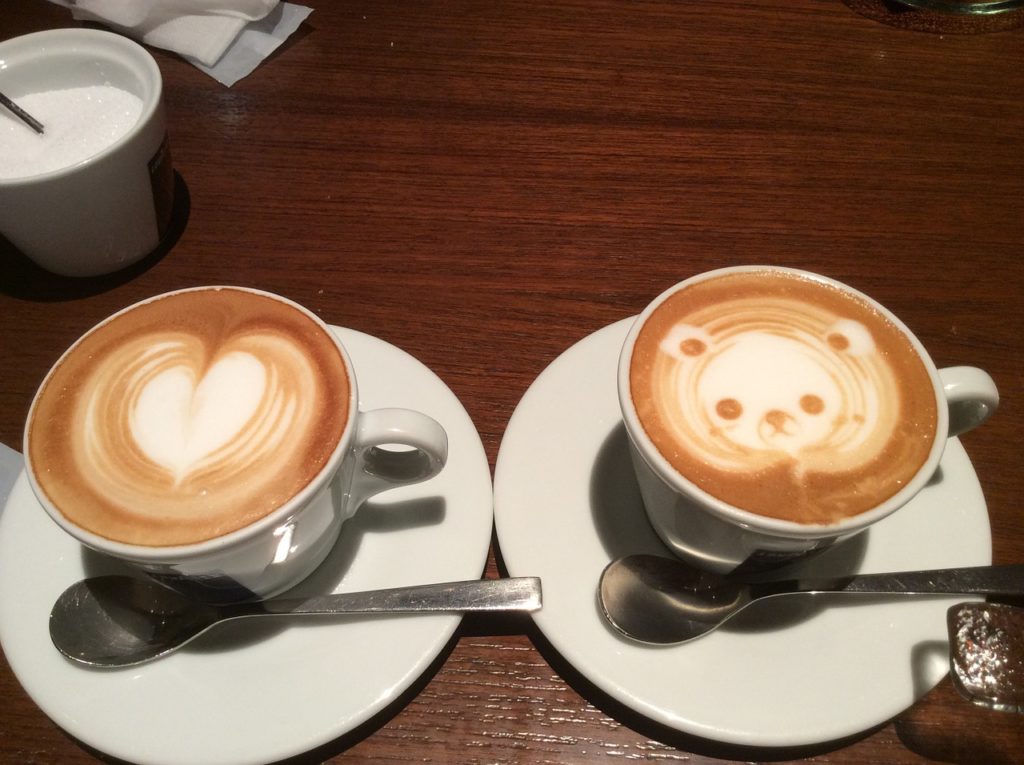 Two cups of espresso sitting on a table. One with heart pattern made of foam and one with a panda made of foam.