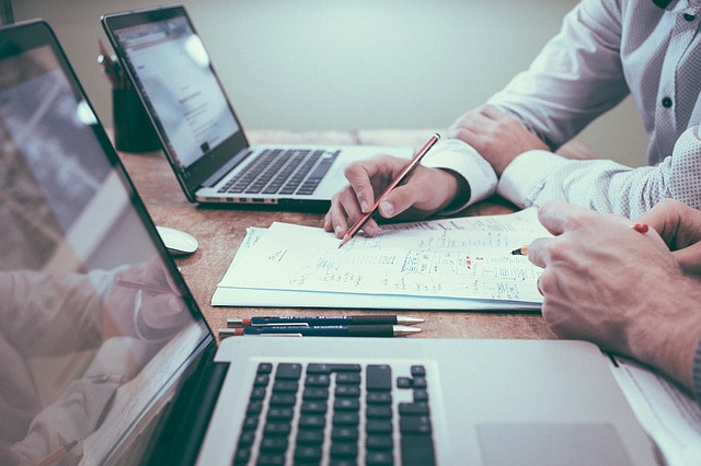 two laptops on a desk and hands of two people meeting