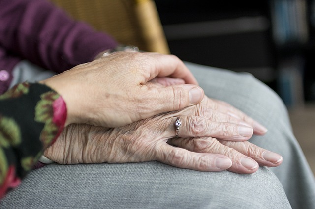 An elderly person having their hands held in a comforting manner