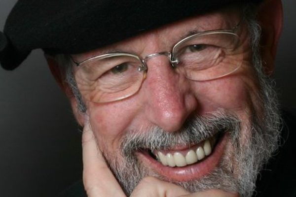 Kelly Thompson, wearing a black beret and smiling, with his chin resting in his hand