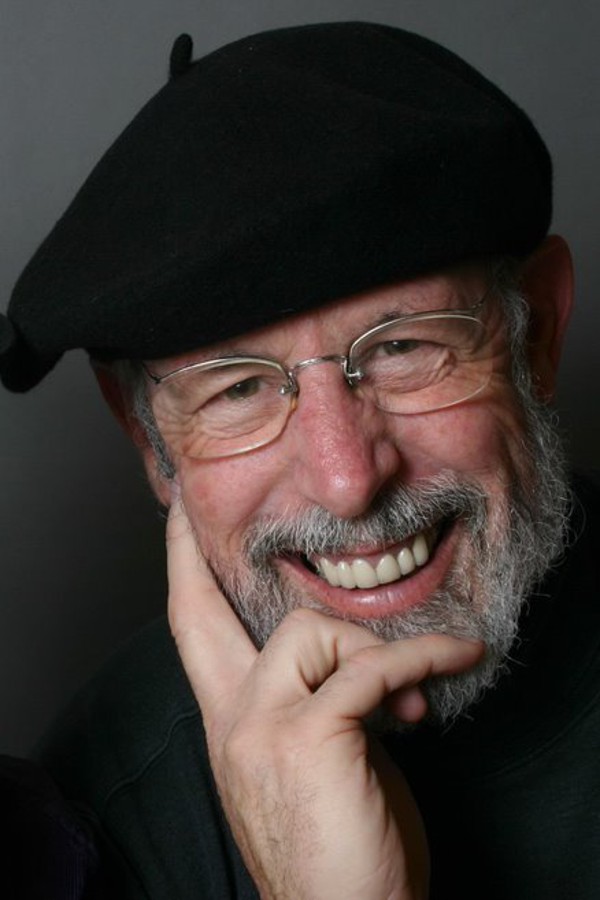Kelly Thompson, wearing a black beret and smiling, with his chin resting in his hand